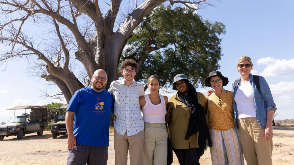 Students and staff members pose in front of jeep and tree